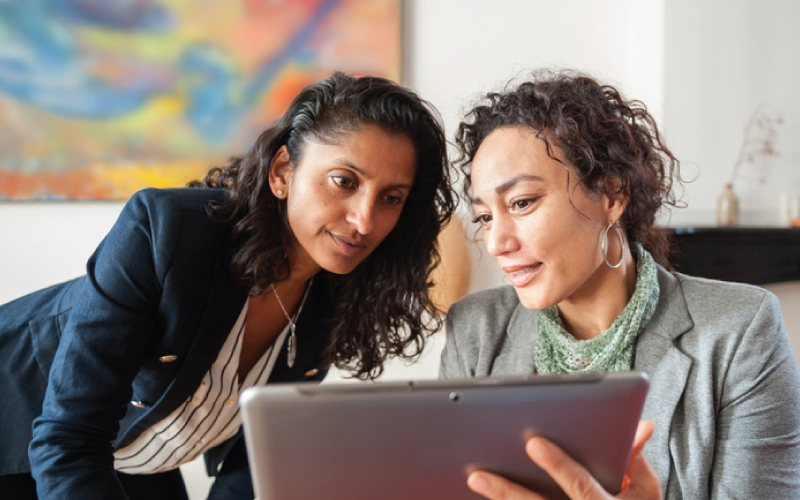 Two female coworkers are reviewing work data information on a tablet