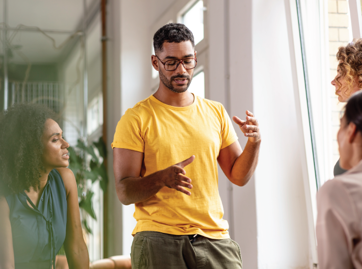 A male employee is discussing the company's sustainability program with his female and male coworkers